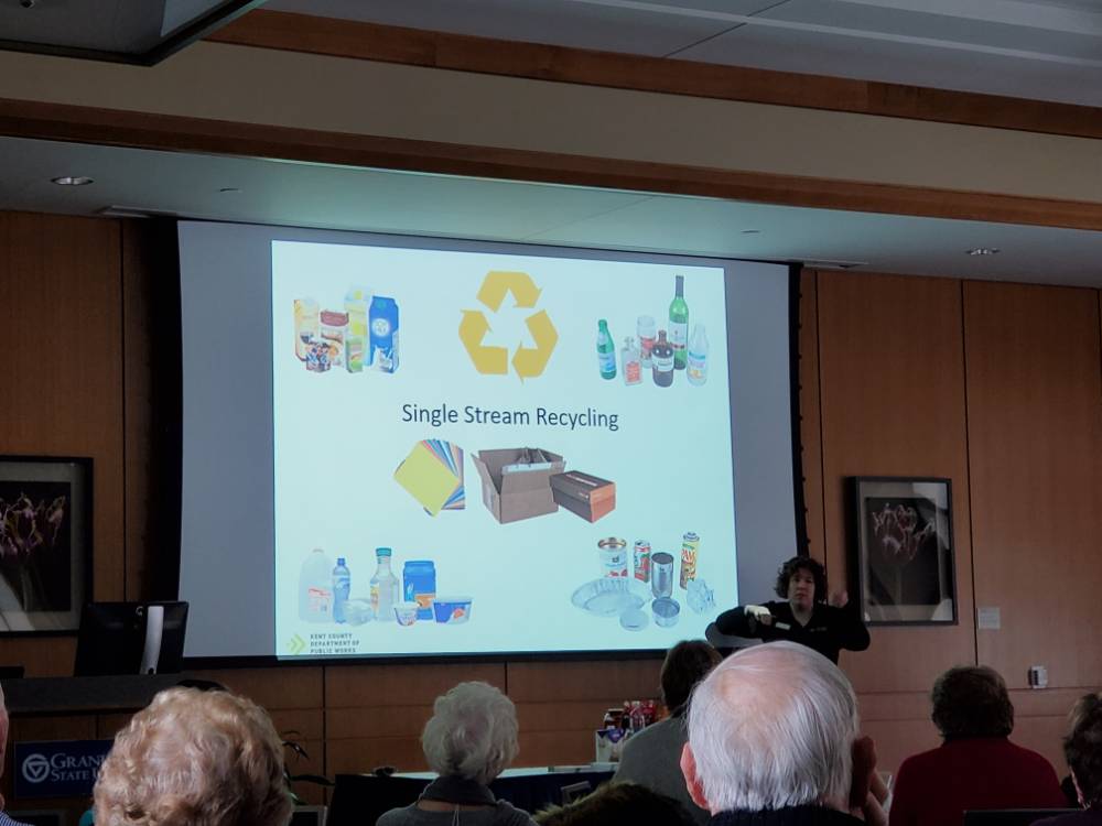 A woman demonstrates in front of a presentation about recycling